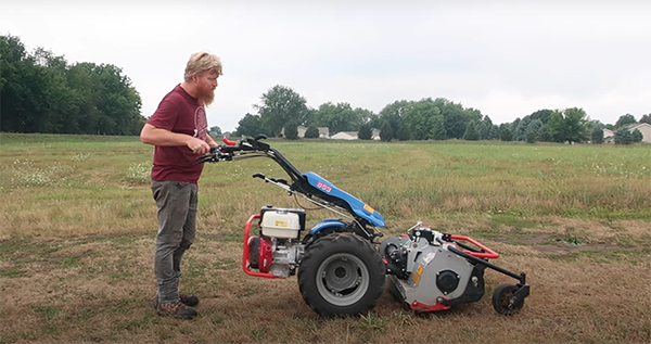 Side view of a farmer attaching a tiller to BCS machine