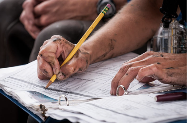 In this photo, a farmer the dirty hands holds a yellow pencil and writes in a recordkeeping notebook.