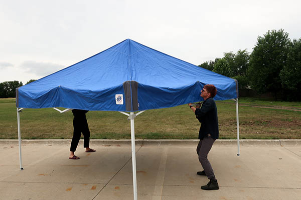 Two people setting up a collapsable tent with a blue roof in an empty parking lot.
