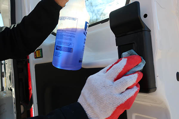 A person wearing gloves holds a spray bottle labeled 