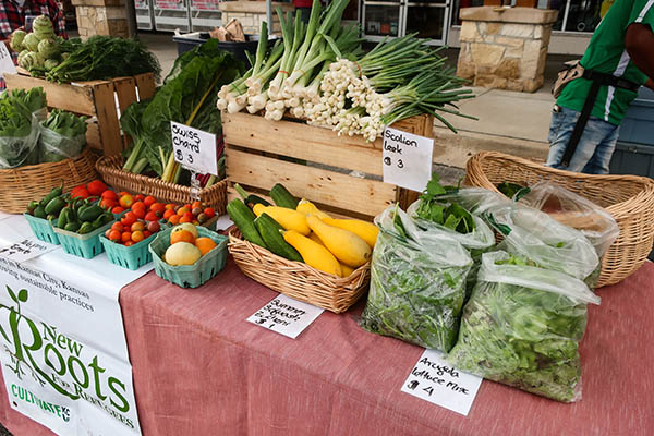 Tomatos, peppers, scallions, leeks, zucchini, squash, and bags of arugula arranged neatly on a farmers market table.