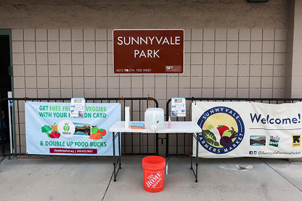 A hand washing station set up on a table in an outdoor park. On the table there are paper towels, microfiber cloths, hand soap, and a water container.