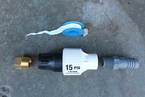 The supplies needed to install a header line to drip tape; a 15 PSI pressure regulator, a ¾ inch by ½ inch brass garden hose adaptor, a ¾ inch PVC Threads x BarbTubing Coupling Adaptor, and 2 hose clamps