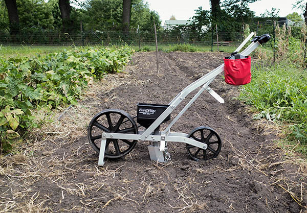 A walk behind seeder parked in front of a plowed field.