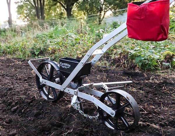 A walk-behind seeder being used in a plowed field.