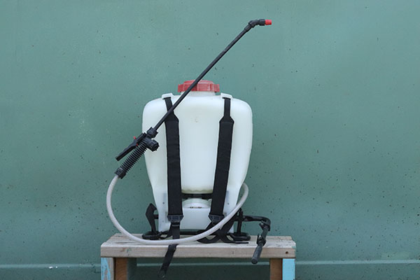Photo of a backpack sprayer has a tank that holds liquid, straps to hold it onto a person's back, and a wand that distributes a fine spray of the liquid.