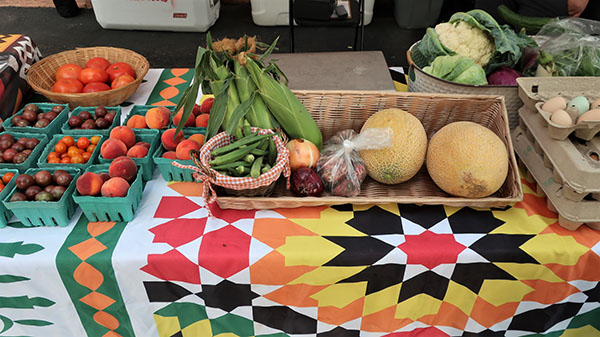 Closeup of a farmers' market display includes melons, corn, tomatoes and okra.